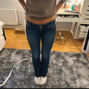 Blå bootcut jeans från Guess - Säljer ett par klassiska blå jeans från Guess med bootcut-passform. Jeansen har låg midja,  snygga detaljer med Guess loggan på bakfickan. Storlek Eu 28. Passar som S/M och 170cm lång. 