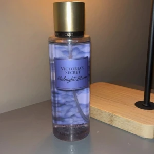 Victoria's Secret Midnight Bloom Body Mist - Fräsch body mist från Victoria's Secret i doften Midnight Bloom. Flaskan är genomskinlig med lila etikett och guldigt lock. Perfekt för dig som gillar blommiga och fräscha dofter.
