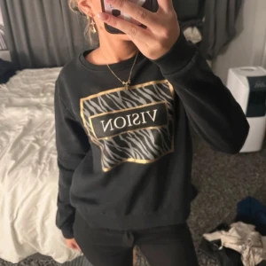 Sweatshirt - Säljer en svart sweatshirt med zebramönster och texten 'VISION' i guld. Tröjan har långa ärmar och en rund halsringning. Perfekt för en avslappnad stil. Strl M🩷