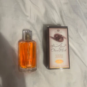 Choco Musk Eau de Parfum - Choco Musk Eau de Parfum från Crown Perfumes kommer i en elegant glasflaska med en varm orange vätska. Doften är söt och chokladig, perfekt för den som älskar gourmanddofter. Förpackningen är stilren med chokladmotiv och text i guld.