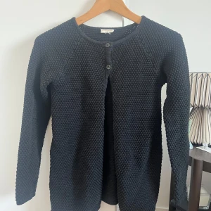 Svart stickad kofta från PompdeLuxe - Snygg svart stickad kofta från PomedeLuxe med rund hals och knappar framtill. Perfekt för kyliga dagar och enkel att matcha med olika outfits. Ett måste i garderoben för en stilren look.