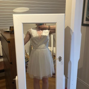 Vit spetsklänning från Moments New York - Säljer en elegant vit klänning från Moments New York. Klänningen har spetsdetaljer och en v-ringad framdel med en öppen rygg. Den är ärmlös och har en kort längd. Har aldrig använt den, lappar kvar