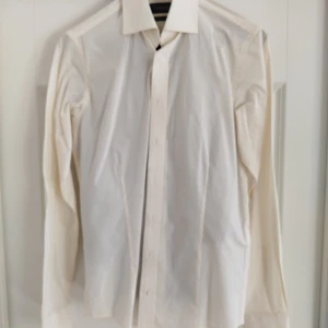 Vit skjorta från Dressmann - Säljer en stilren vit skjorta från Dressmann Premium Collection. Skjortan är tillverkad i bomull med stretch för extra komfort och har långa ärmar samt knappar framtill. Perfekt för en elegant look.