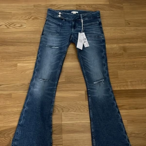 Blå bootcut jeans med slitningar - Snygga blå bootcut jeans med slitningar på framsidan. De har en låg midja och stängs med två knappar och dragkedja. Perfekta för en avslappnad stil med en modern touch. Passar mig i längden som 159. Helt slutsålda i flesta butiker + online, priset är diskuterbart 💓