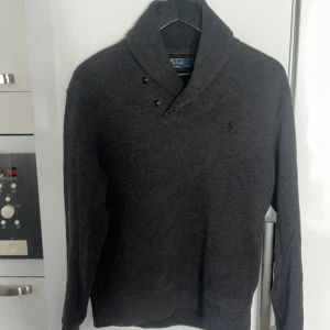 Mörkgrå tröja från Polo Ralph Lauren - Säljer en stilren mörkgrå tröja från Polo Ralph Lauren med knappar vid kragen och bruna armbågslappar. Perfekt för en klassisk look. Tröjan har långa ärmar och en mjuk känsla. Har använt den 1-2 gånger och är i super bra skick! Pris kan diskuteras 👍