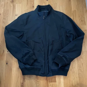 Mörkblå jacka från Polo Ralph Lauren - Säljer en stilren svart jacka från Polo Ralph Lauren i storlek M. Skitnice material och passform. Jackan har en dragkedja framtill och två fickor med dragkedja. Den är långärmad och har en diskret broderad logga på bröstet. 