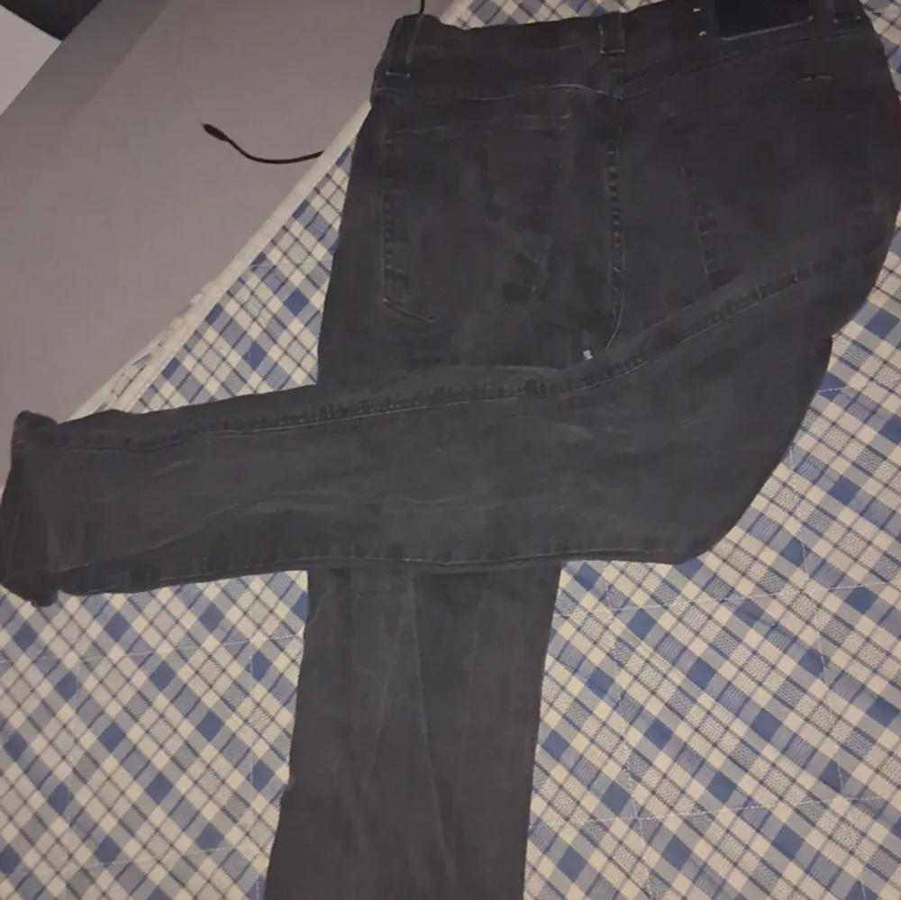 Snygga svarta jeans från Nudie Jeans med klassisk femficksdesign. De har en knappgylf och subtila orangea detaljer vid fickorna. Perfekta för en stilren look.. Farkut & Housut.