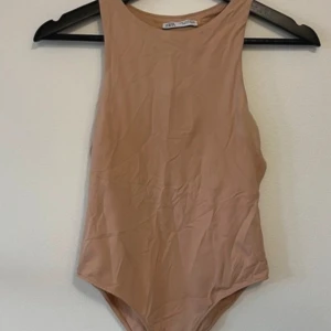 Zara Beige ärmlös bodysuit - Säljer en stilren Zara  beige bodysuit med ärmlös design. Perfekt för att matcha med olika outfits. Materialet är mjukt och stretchigt för en bekväm passform.
