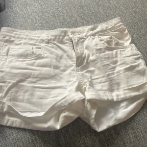 Vita shorts med fickor - Säljer ett par vita shorts med fickor fram och bak. De har en klassisk design med knapp och dragkedja framtill. Perfekta för varma dagar!