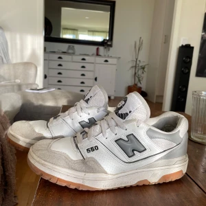 New Balance 550 sneakers - Säljer ett par New Balance 550 sneakers i vitt och grått med svarta detaljer. Skorna har snörning och en robust sula i gummi. Perfekta för en avslappnad stil.