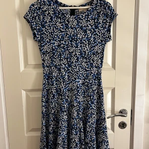 Blommig klänning från Michael Kors - Säljer en söt blommig klänning från Michael Kors i blått och vitt. Klänningen har korta ärmar och en rund halsringning. Perfekt för en somrig look! 🌸