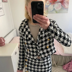 Svartvit rutig kavaj från Stories - Säljer en stilren svartvit rutig kavaj från Stories. Kavajen har en croppad passform med guldknappar framtill. Tillverkad i 100% polyester, perfekt för en chic look. Passar utmärkt för både vardag och festliga tillfällen.