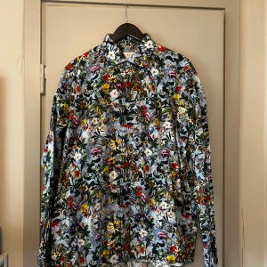 Blommig skjorta från Eton - Säljer en färgglad blommig skjorta från Eton i passform “Contemporary“ storlek 43/XL. Skjortan har ett livfullt mönster med blommor i olika färger på en ljus bakgrund. Perfekt för att liva upp garderoben med lite färg och stil. Den har långa ärmar och knappar framtill.