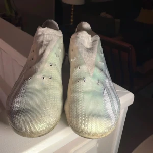 Adidas Fotbollsskor - Snygga fotbollsskor med en futuristisk design. Skorna har en vit och silver färgkombination med diskreta svarta detaljer. Perfekta för snabba rörelser på planen.