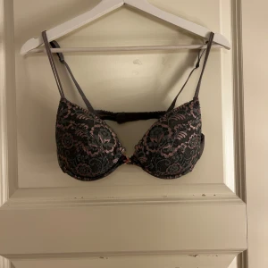 Grön och rosa spets-bh - Elegant bh i grönt med rosa spetsdetaljer. Den har justerbara axelband och en klassisk knäppning bak. Perfekt för att lägga till en touch av lyx till din underklädeskollektion.