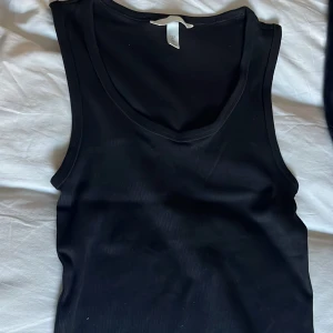 Svart ribbad linne från H&M - Säljer en stilren svart ribbad linnetopp från H&M. Perfekt för lager-på-lager eller att bära som den är. Den är nästan aldrig använd o som ny💕