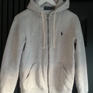 Grå hoodie från Ralph Lauren - Säljer en stilren grå hoodie från Ralph Lauren med dragkedja och klassisk logga på bröstet! Skick 8/10, Storlek XS, Köpt på Zalando