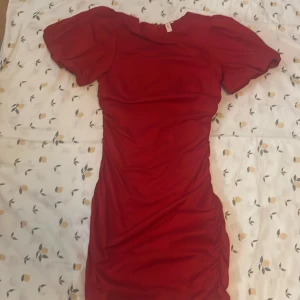 Röd klänning från Nelly - Snygg röd klänning från Nelly med puffiga kortärmar och en figurnära passform. Klänningen har en dragkedja i sidan och är perfekt för en kväll ute. Den är gjord i ett mjukt och stretchigt material.