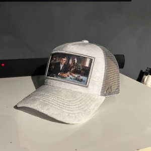 Maggiore keps - Snygg vit keps med en unik broderad patch framtill. Kepsen har ett nätmaterial på baksidan för bättre ventilation och en justerbar rem för perfekt passform. Nypris 800kr aldrig använd 