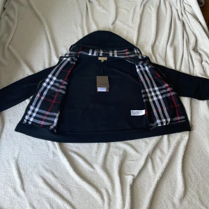 Svart hoodie från Burberry - Snygg svart hoodie från Burberry med dragkedja och klassiskt rutigt mönster i huvan. Den är 10/10    Är en L men passar bäst för M inga skador rekommenderar stark