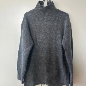Grå stickad tröja - Mysig grå stickad tröja med ribbade detaljer vid ärmslut och nederkant. Lite längre i modellen, med slit längst ner på båda sidor. Endast använd fåtal gånger!