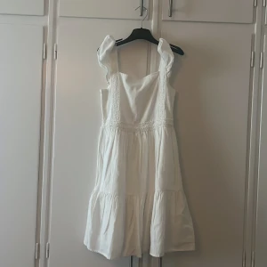 Vit klänning med broderade detaljer från Mango - Supersöt vit klänning från Mango med breda axelband och fina broderade detaljer framtill. Klänningen har en luftig passform och volang nertill, perfekt för varma dagar.