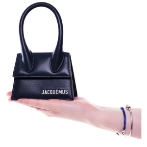 Svart minihandväska från Jacquemus - Superstylish svart minihandväska från Jacquemus med ett unikt, skulpturalt handtag och minimalistisk design. Väskan är tillverkad i slätt skinn och har en tydlig logga framtill. Perfekt accessoar för att lyfta din outfit.