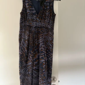 Mönstrad omlottklänning från Fall Winter Spring Summer - Säljer en snygg omlottklänning från Fall Winter Spring Summer i storlek 36. Klänningen har ett unikt mönster i blått och brunt, är ärmlös och har en v-ringad omlottdesign. Perfekt för dig som vill sticka ut med stilren look.