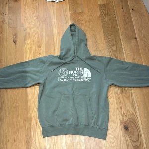 Grön hoodie från The North Face - Säljer en grön hoodie från The North Face med vit logga och tryck framtill. Tröjan har huva med magficka. Perfekt för en avslappnad stil. Köpt för 700+ men säljer för 250