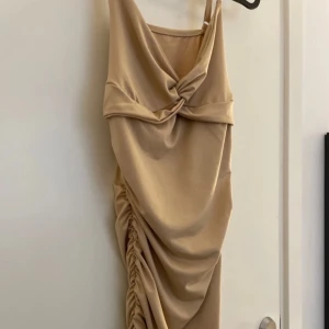 beige klänning med drapering - Säljer en elegant långklänning i champagnefärg med snygg drapering och twistad detalj framtill. Klänningen har smala axelband och en åtsittande passform med rynkade sidor för en extra fin look💞