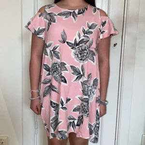 Rosa blommig klänning med cut-out axlar från Lindex - Säljer en söt rosa klänning från Lindex med stora svartvita blommor och trendiga cut-out axlar. Klänningen har korta ärmar och en avslappnad passform, perfekt för sommarens alla tillfällen. Superfin och bekväm modell!