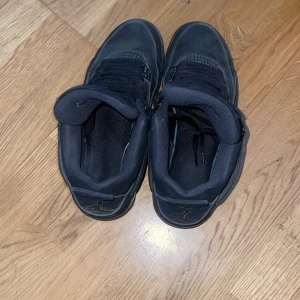Black Cats Jordan 4s - Säljer ett par helsvarta Nike Air Jordans sneakers med klassisk siluett och rund tå. Skorna har snörning och är tillverkade i skinn med detaljer i syntet. Perfekta för dig som gillar streetwear och vill ha en ikonisk look. Skorna är äkta. 