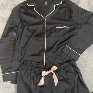 Pyjamas från Bluebella - Silkeslen pyjamas från Blubella i svart med ljusrosa detaljer i storlek S. Oanvänd och därmed i nyskick.