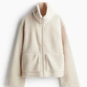 Beige teddyjacka med dragkedja - Mysig beige teddyjacka med hög krage och dragkedja framtill. Jackan har två stora fickor och är perfekt för kyligare dagar. Passformen är normal och materialet är mjukt och fluffigt.