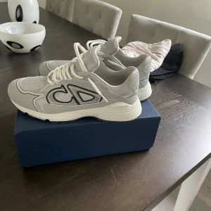 Dior b30 - Säljer ett par gråa Dior sneakers med vit sula och stora svarta CD-detaljer på sidan. Skorna har snörning och är tillverkade i en kombination av mesh och syntetmaterial. Perfekta för dig som gillar stilrena och exklusiva sneakers. Stolek 45 men passar perfekt om du har Strolek 44 då jag har de , använda ca 4-5 gånger . 
