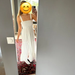 Vit långklänning med volang - Säljer en vit långklänning med breda axelband och smockad överdel. 