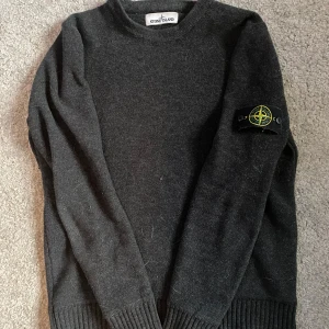 Stone Island stickad tröja  - Säljer en mörkgrå stickad tröja från Stone Island. Tröjan har Stone Island-loggan på vänster ärm. Litet hål på vänsterarmern syns knappt. Skick 7/10