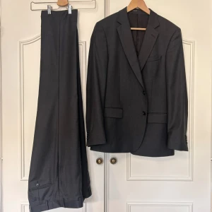 Mörkgrå måttsydd kostym med TRE PAR BYXOR - Säljer en mörkgrå måttsydd kostym i modell Paris, med tyg från Vitale Barberis Canonico. Motsvarar ungefär storlek herr 50. Eftersom den är måttsydd är Fredrik Andersson broderat på insidan av kavajen men det är inget som syns när man har på sig den. Orginalpris ca 10 000kr. Det är en kavaj och tre par byxor.