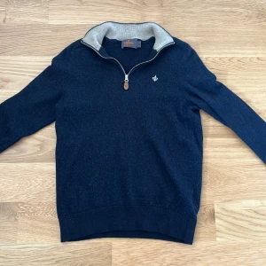 Mörkblå merinoullströja med dragkedja från Morris - Säljer en stilren mörkblå tröja från Morris i 100% merinoull. Tröjan har halv dragkedja vid kragen, En snygg logga på bröstet och ribbade muddar. Perfekt för lite kyligare dagar. Tröjan har blivit mindre under tiden och skulle nu säga att den är i storlek xxs, kommer någ att passa perfekt för någon som är mellan 150-155 cm lång. Om du funderar över något är det bara att fråga.