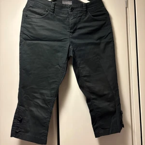 Svarta trekvartsbyxor från Esprit - Svarta trekvartsbyxor från Esprit med normal passform. Byxorna har knappar som detalj vid bensluten och klassisk femficksdesign. Perfekta för dig som vill ha en stilren och enkel look med lite kortare ben.