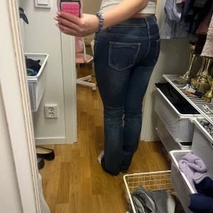 Mörkblå utsvängda jeans  - Säljer ett par mörkblå jeansbyxor med utsvängd stil med diskreta slitningar för en snygg look. Perfekta till vardags och lätta att matcha med olika toppar.