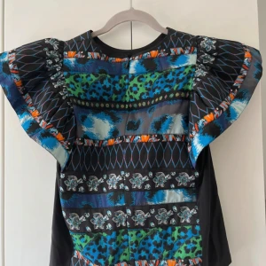 Färgstark mönstrad top från Kenzo - Unik top från Kenzo i samarbete med H&M. Korta volangärmar och mixade mönster i blått, grönt, svart och orange med inslag av leopardmönster, blommor och grafiska detaljer. Materialet känns slätt och glansigt, perfekt för dig som vill sticka ut.