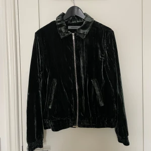 Mörkgrön velourjacka med dragkedja - Säljer en mörkgrön velourjacka från Maniére De Voir med dragkedja framtill och klassisk krage. Jackan har två snedställda fickor och resår vid midjan och ärmslut. Perfekt för dig som vill ha en unik och stilren look. Mått: 58 cm lång, arm utv 60cm, arm inv 45cm, bröstvidd 38cm, rygg 45cm.