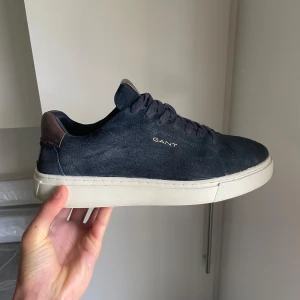 Mörkblå sneakers från Gant i mocka - Säljer ett par stilrena mörkblå sneakers från Gant i mocka med vit platt sula och bruna detaljer vid hälen. Har använts få månader. Perfekta för en avslappnad och snygg look. Kontakta för mer bilder o info 