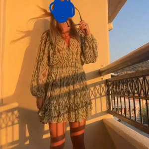 Grön mönstrad kortklänning med volang - Kort klänning i ljusgrönt med bohemiskt mönster och långa ärmar. Klänningen har markerad midja, v-ringning och volangdetaljer nertill. Perfekt för varma dagar och har en luftig känsla. Bilderna tagit från min tiktok💞💞