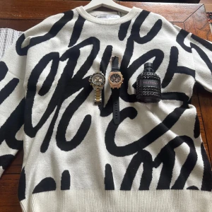 Trendigt stickad tröja från Bershka (S/M) – Ny! - Sätt stilen med denna snygga och bekväma knit sweater från Bershka i storlek S/M. Fräsch vit bas med svart grafiskt mönster som drar blickarna till sig – perfekt för dig som gillar att sticka ut med stil! Tröjan är helt ny med tag kvar.  OBS! Klockor och parfym i första bilden är endast med för styling – ingår ej i köpet. 