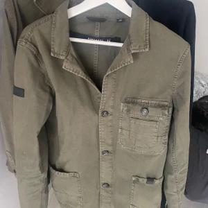 Olivgrön superdry overshirt/field jacket  - Säljer en olivgrön overshirt från Superdry med klassisk krage och knappstängning. Jackan har tre fickor framtill, varav en bröstficka med knapp. Perfekt som overshirt eller fieldjacket 