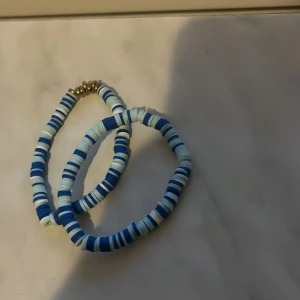 Blått och vitt pärlarmband - Två armband med platta pärlor i olika nyanser av blått och vitt. Armbanden har elastisk tråd och små guldfärgade detaljer vid låset. Perfekt för att addera lite färg till din outfit.