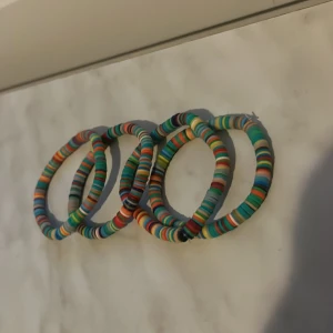 Färgglada armband i plast - Fyra stycken armband i plast med färgglada ränder i blått, orange, grönt, vitt och rött. Perfekta för att addera lite färg till din stil. Säljs som ett set.