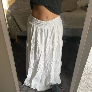 Vit långkjol med resårmidja - Säljer en vit långkjol med bred resår i midjan. Kjolen har en luftig och flowy passform, perfekt för varma dagar. Enkel och stilren design utan mönster eller extra detaljer. Passar dig som gillar en avslappnad och bekväm stil. 